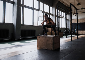 Fit young woman box jumping at a crossfit style gym. Female athlete is performing box jumps at gym.