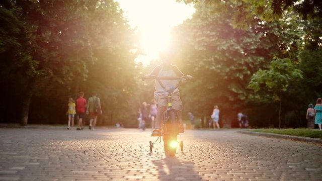 Child riding bicycle in park at sunset light. Kid in helmet learning to ride at summer. Happy boy riding bike, having fun outdoors on nature. Active sport family leisure. Healthy holidays. Slow motion