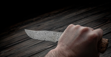 Hunting bowie knife with a wooden handle on dark wooden background. Steel arms weapon. top view