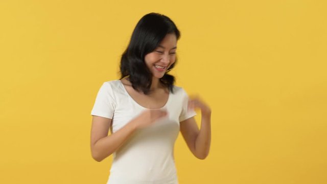 Beautiful smiling young Asian woman opening palms and pointing her finger to copy space over yellow background