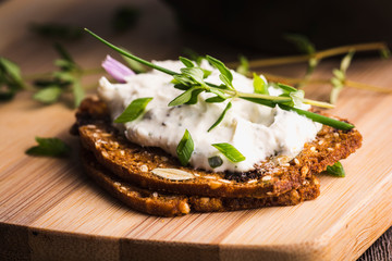 A delicious garlic and chive cream cheese spread on herbed crackers stacked on a bamboo cutting board.