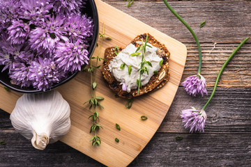 A delicious garlic and chive cream cheese spread on herbed crackers next to a bowl of purple chive flowers.