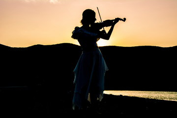 Silhouette of woman playing violin at beach with sunset background