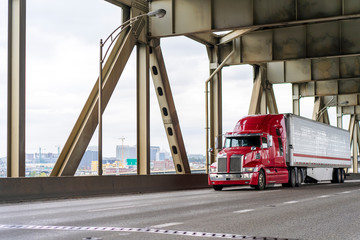 Bright red big rig semi truck transporting cargo in refrigerator semi trailer moving on the two levels bridge across Willamette River in Portland