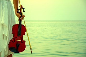 Woman holding violin at sunset on beach © Aycan