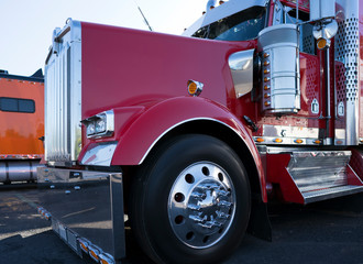 Shiny red big rig semi truck tractor with chrome parts and accessories standing on truck stop parking lot