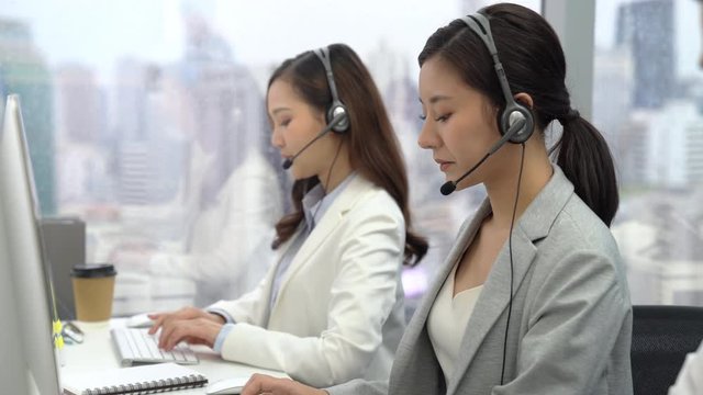 Beautiful woman Asian customer service operators talking on headsets and using computer at call center office with team