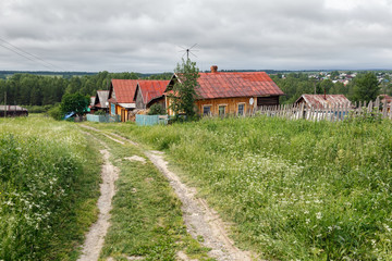 Village street in summer, overgrown with grass and flowers. View of the traditional wooden rural houses. Village of Visim, Sverdlovsk region, Urals, Russia