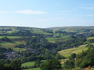 a panoramic view of the village of luddenden in west yorkshire surrounded by fields mills and trees in summer sunlight