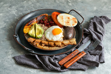 Colombian food. Bandeja paisa, typical dish at the Antioquia region of Colombia - chicharrón (fried pork belly), black pudding, sausage, arepa, beans, fried plantain, avocado egg, and rice.