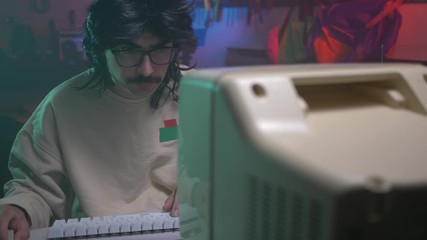 In the '80s or '90s young man using his personal computer typing on a keyboard. Retro scene with vintage colors and atmosphere.
