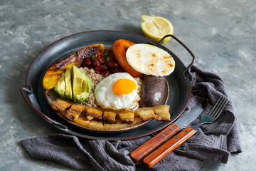 Colombian food. Bandeja paisa, typical dish at the Antioquia region of Colombia - chicharrón (fried pork belly), black pudding, sausage, arepa, beans, fried plantain, avocado egg, and rice.