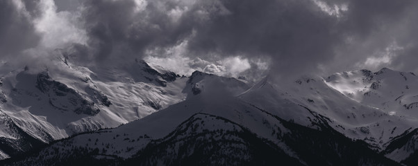 Panorama of Dramatic Snow Covered Alpine Peak Surrounded by Storm Clouds