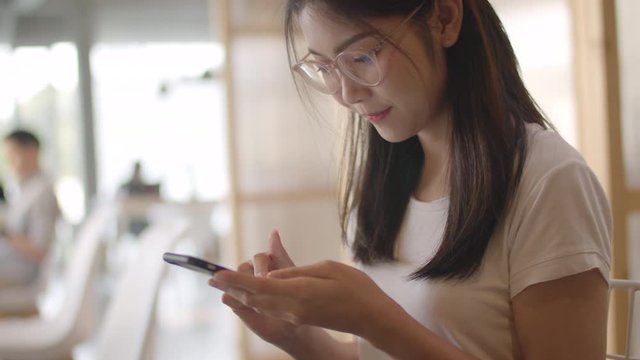 Freelance Asian women using mobile phone at office. Young Japanese Asia Girl using smartphone checking social media on the internet on the table at workplace concept. Slow motion.