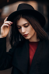 beautiful young woman in a black coat and hat looks in the frame