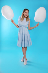 Full length portrait of pretty young woman with tasty cotton candy on blue background