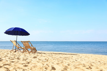Empty wooden sunbeds and umbrella on sandy shore. Beach accessories