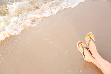 Closeup of woman with stylish flip flops on sand near sea, space for text. Beach accessories