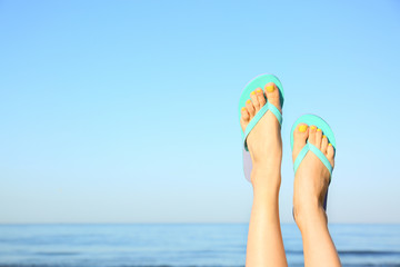 Closeup of woman wearing flip flops near sea, space for text. Beach accessories