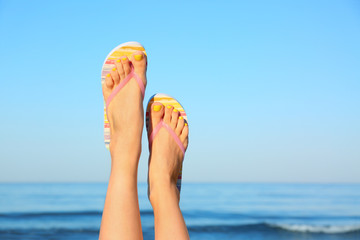 Closeup of woman wearing flip flops near sea, space for text. Beach accessories