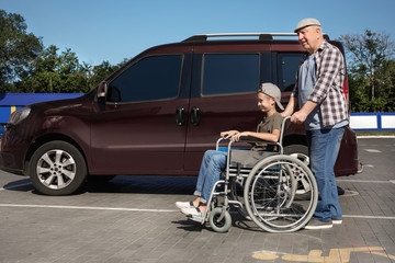 Senior man with boy in wheelchair near van on car parking
