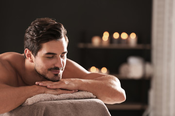 Handsome young man relaxing on massage table in spa salon, space for text