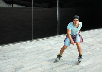 Handsome young man roller skating near glass building on city street, space for text