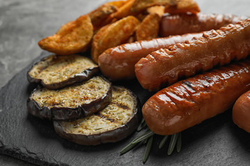 Delicious grilled sausages and vegetables on slate plate, closeup. Barbecue food