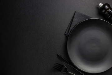 Black setting: plates, linen napkin and silverware on blfck background. Top view.