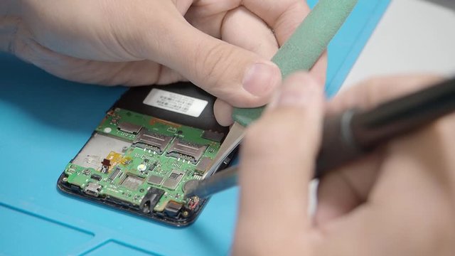 Smartphone assembling in repair shop. Soldering contact on circuit board with the soldering iron. Mobile phone maintenance service