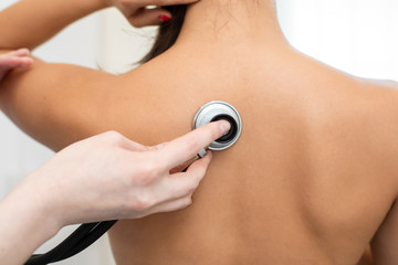 Woman doctor therapist listening with a stethoscope to a back, young female patient