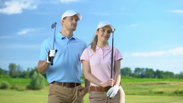 Confident male and female golf players with clubs looking at course, sport game - Powered by Adobe