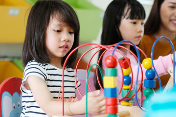 Cute asian girl playing toy in kindergarten classroom, Asian elementary, pre school kid and teacher happy with toys in classroom, kid education concept