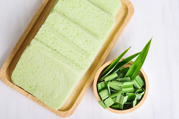 Sliced pandan bread on wooden plate and pandan leaf, top view