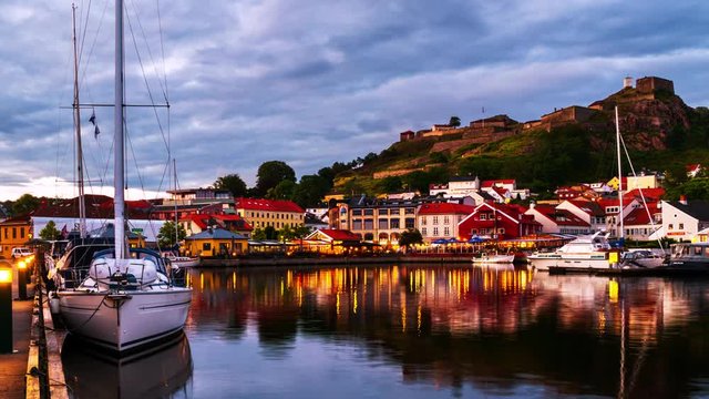 Halden, Norway. View of the illuminated houses and yachts with Fredriksted fortress at the background. Time-lapse at sunset with cloudy sky in summer, panning video