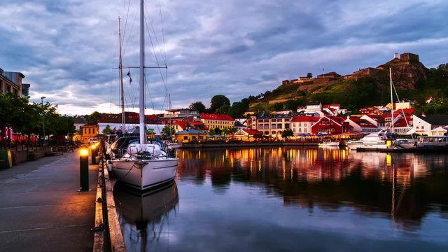 Halden, Norway. View of the illuminated houses and yachts with Fredriksted fortress at the background. Time-lapse at sunset with cloudy sky in summer, zoom in