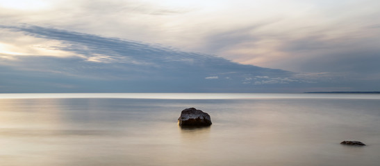 Fototapeta na wymiar Single rock in smooth water with clouds North beach Ontario Canada