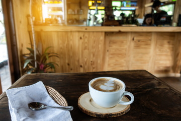 The ceramic cup of hot cappuccino coffee on the wooden table in the restaurant or coffee shop. natural light. morning hot drink cafe shop.