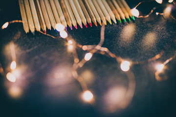 set of coloured pencils on desk with fairy lights shot at shallow deph of field