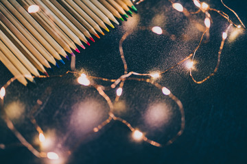 set of coloured pencils on desk with fairy lights shot at shallow deph of field