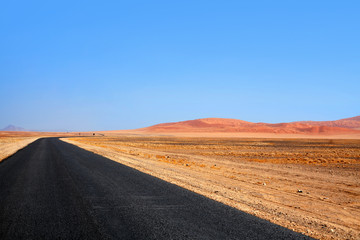 Fototapeta na wymiar Empty black asphalt long road, Namib desert dunes and blue sky background, transportation design template, nobody, beautiful rural lonely landscape panoramic view, African travel concept, copy space