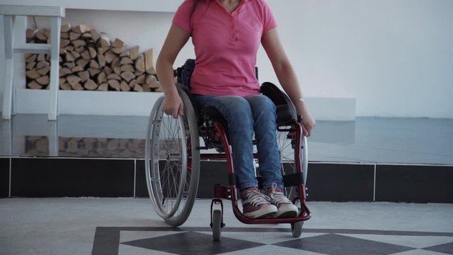 Young disabled female wearing in denim jeans clothes sitting in special invalid chair or handicap in house with bright and soft light room. Woman in comfort wheelchair spending day at home