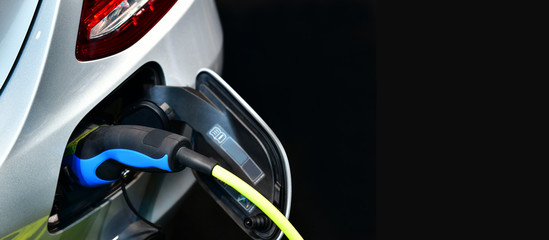 Electric Vehicle charging in station with power supply plugged into an electric car being...