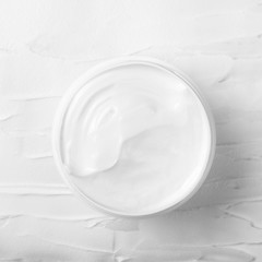 Fototapeta na wymiar Open white jar with white face cream on a background of smeared cream. Cosmetic moisturizing product. Top view, flat lay.