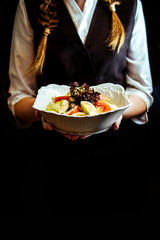 In the hands of the waiter on a plate is a salad of fresh vegetables