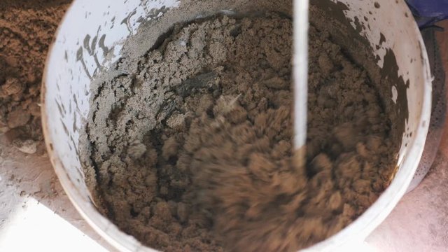 Construction worker mixing concrete with water with drill for building. Close up mixed cement in a mortar bucket