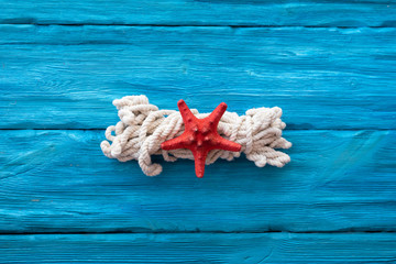 Mooring rope and red starfish on blue wooden table background. Sea travel concept.