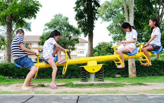 Happy Asian children playing seesaw board together in the park outdoor, lifestyle concept.