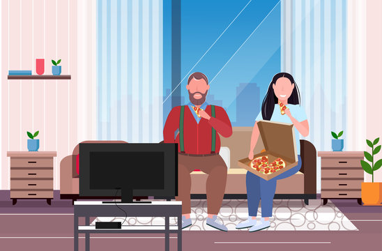 fat obese couple eating pizza fast food overweight man woman watching tv sitting on couch unhealthy nutrition obesity concept modern living room interior full length flat horizontal