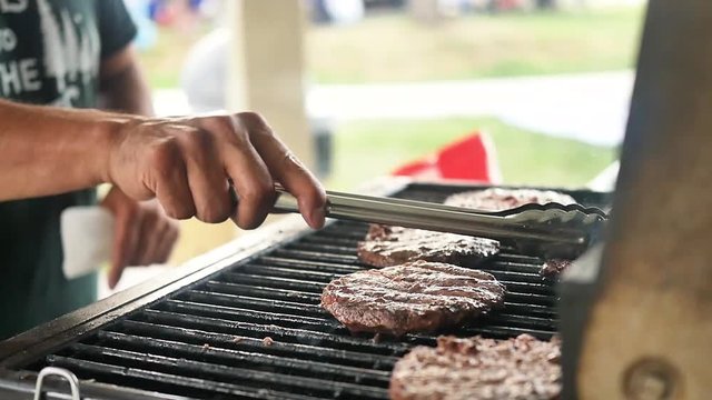 Slow motion shot of beef patty being flipped with tongs as flames rise up from the grill